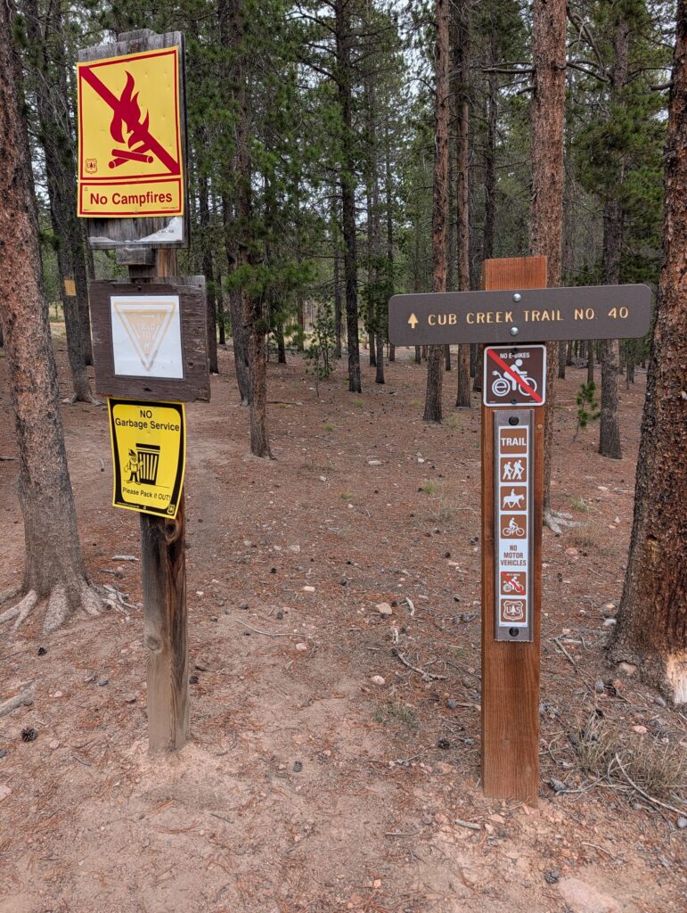 A brown trail post reading Cub Creek Trail No. 40 with a No E-Bikes sign and symbols for hikers, horses and bicycles, no motor vehicles.