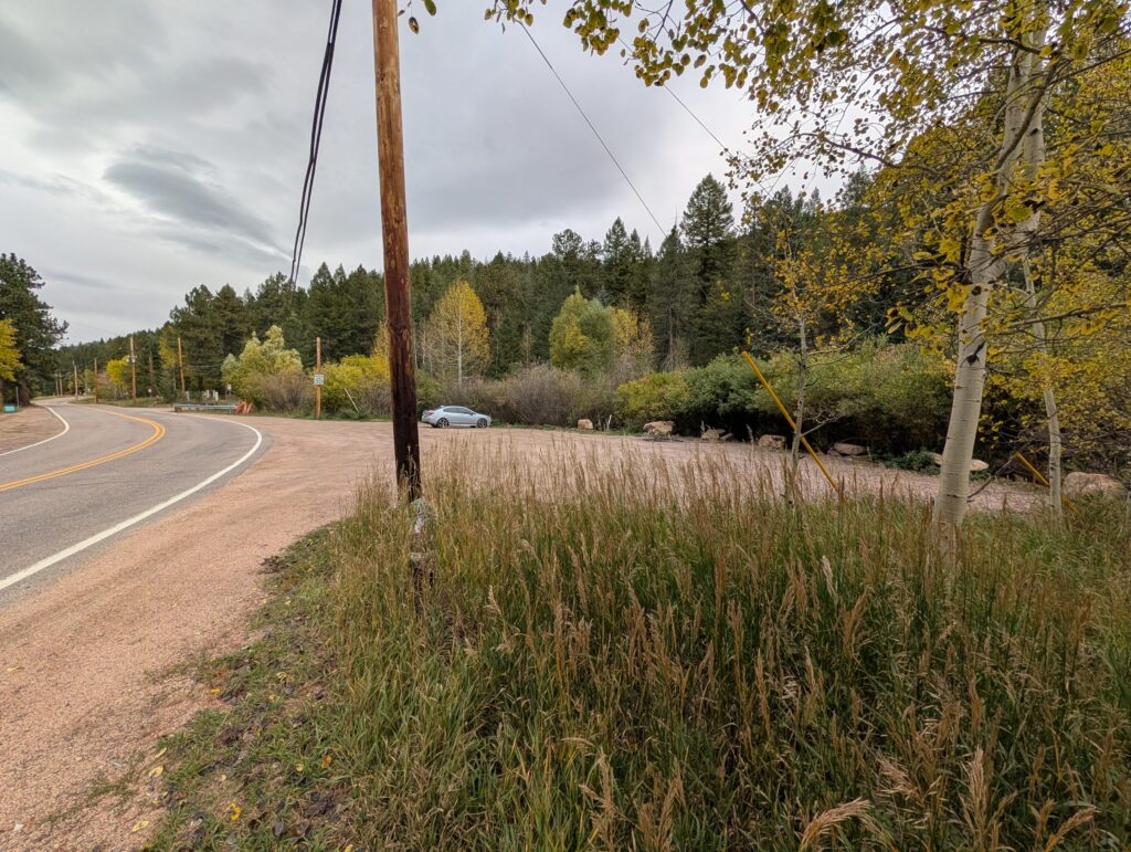 A wide gravel pull-off beside Brook Forest Road with one car parked, edged with grass and aspens.