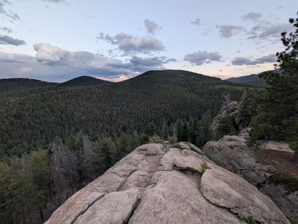 Evening clouds over rolling forested hills, seen from a broad granite outcrop.