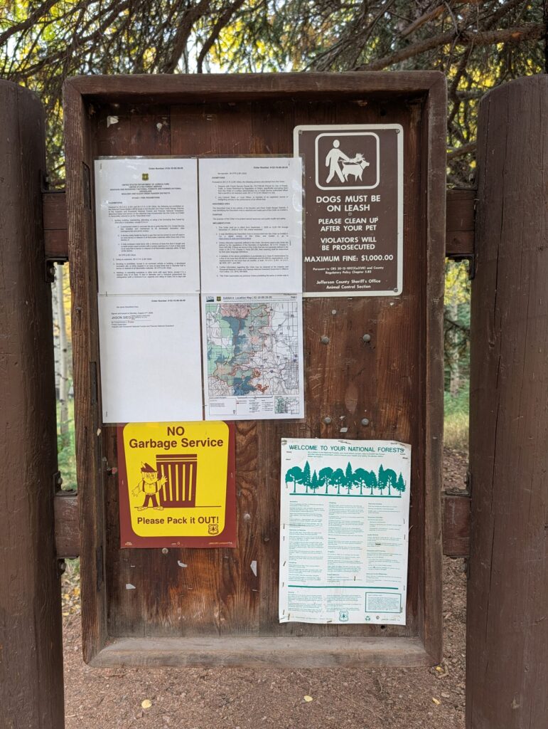 The upper trailhead kiosk with a leash-law sign, posted orders and map, and a No Garbage Service sign.
